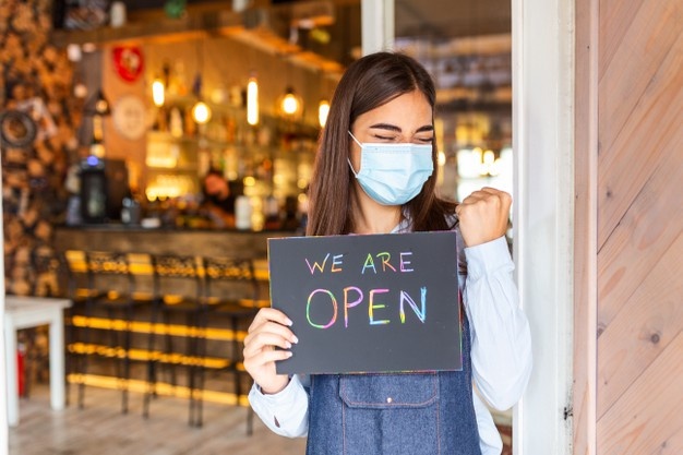 happy-female-waitress-with-protective-face-mask-holding-open-sign-while-standing-cafe-restaurant-doorway-open-again-after-lock-down-due-outbreak-coronavirus-covid-19_1212-2948